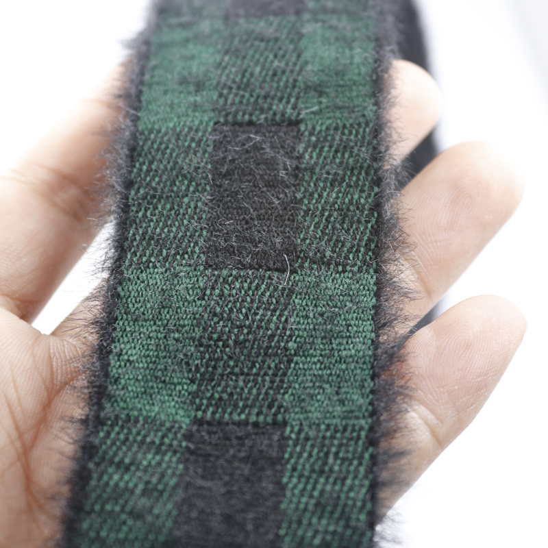 Hand holding a length of faux mink velvet plaid elastic band, showing the green base with black check pattern against the palm