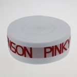 Flat coiled roll of white jacquard elastic webbing with red SENSON PINKY branding around the edge