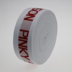 Upright roll of white jacquard elastic band with red SENSON PINKY lettering, viewed from the side