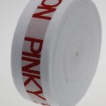 Angled view of a white jacquard elastic roll with red PINKY lettering and tightly wound layers