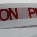 Close-up of white jacquard elastic showing red woven ON and PI letters and fine knit texture