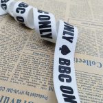 White ribbon with black BBC ONLY print and spade symbol, coiled in a loose loop on printed newspaper