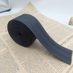 Rolled navy blue herringbone twill polyester webbing on newspaper, showing the dense woven surface and cut end