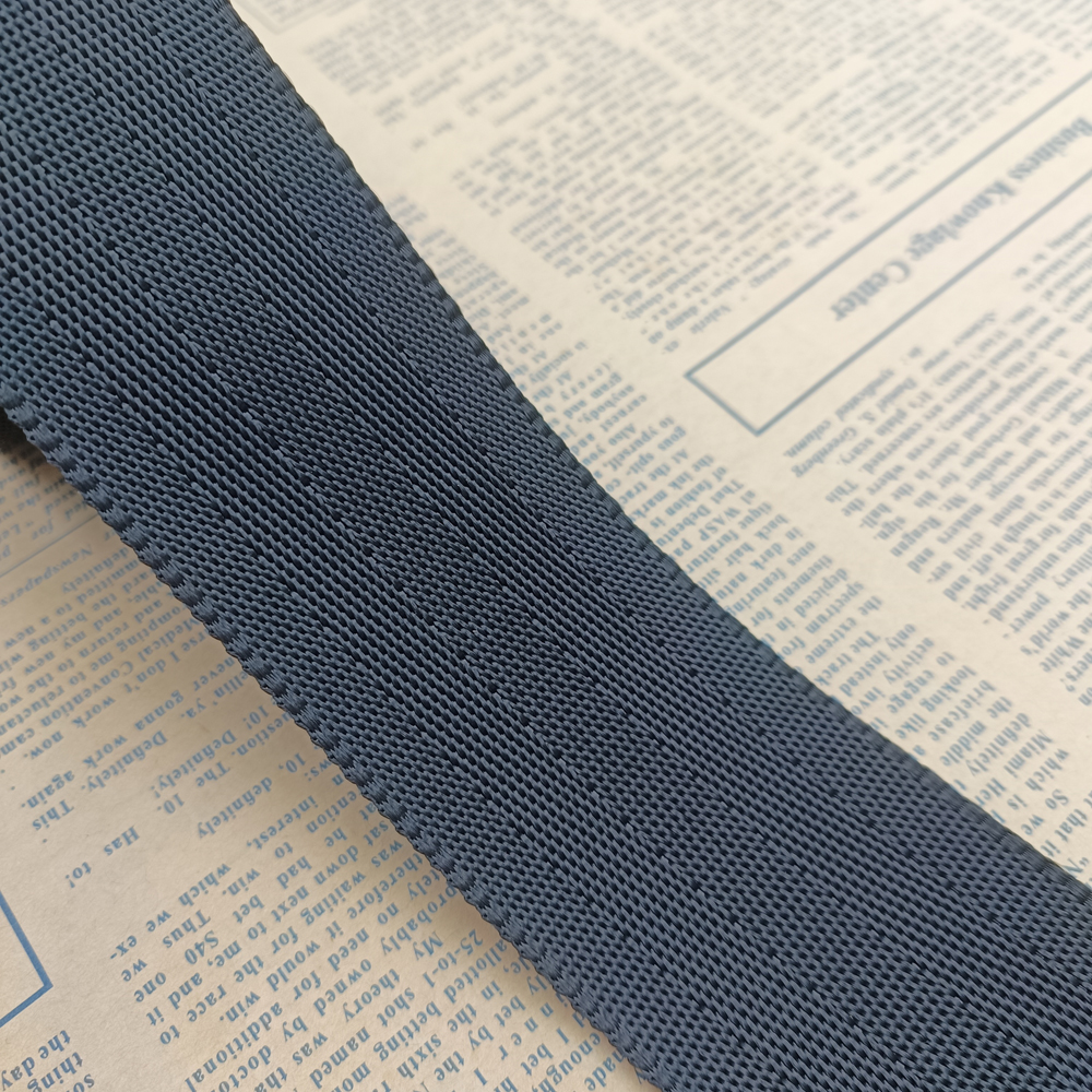 Close-up of dark blue polyester webbing with fine herringbone twill weave and a clean woven edge on newspaper