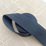 Navy blue polyester webbing looped into a soft curve on newspaper, showing the herringbone weave and edge