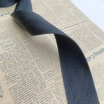 Dark navy webbing folded into a loop on newspaper, revealing the herringbone twill pattern and firm hand