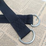 Black polyester webbing strap with two silver metal D-rings attached by stitched folds, on newspaper