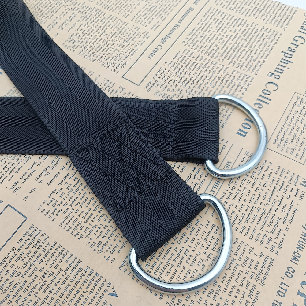 Black polyester webbing strap with two silver metal D-rings attached by stitched folds, on newspaper