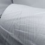 Close-up of white woven sealing strip material with a visible grid texture, partially covered by clear plastic film