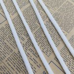 Several white braided sealing strips laid diagonally across a printed newspaper page, showing their textured surface