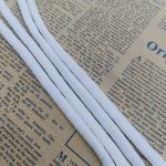 White braided sealing strips arranged in parallel lines on a newspaper page, highlighting the woven texture and shape