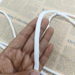 Hand holding a white braided sealing strip with a textured surface, shown close up against a newspaper background