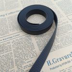 Coiled black PVC-coated webbing strap with honeycomb embossed texture resting on printed newspaper sheets