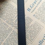 Close-up of a black PVC-coated webbing strap with raised honeycomb pattern laid vertically across printed newspaper pages