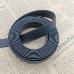Neatly wound roll of black honeycomb-textured PVC-coated webbing strap on printed newspaper, showing layered edges
