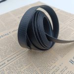 Rolled black PVC-coated webbing strap with honeycomb texture, loose end curling outward on a newspaper background