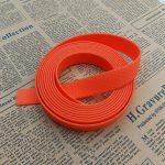 Roll of bright orange PVC-coated webbing strap with honeycomb texture, loose end folded outward on newspaper