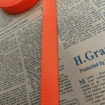 Close-up of orange PVC-coated webbing strap with raised honeycomb pattern running vertically over printed newspaper text