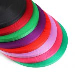Close-up of stacked woven webbing rolls in black, red, green, purple, pink and teal showing ribbed edges
