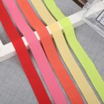 Elastic binding tape in coral red, orange, pink and lime green arranged in a fan