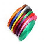 Stack of woven webbing rolls in orange, blue, yellow, red, purple, pink and green arranged on a white background