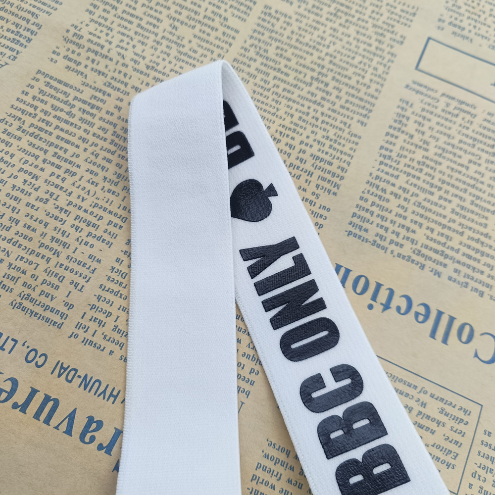 Folded white webbing strap with black BBC ONLY lettering and spade icon, resting on newspaper text