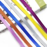 Six woven webbing straps in blue, white, yellow, purple, orange and pink laid over a book on a white background