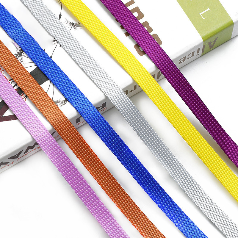 Six woven webbing straps in blue, white, yellow, purple, orange and pink laid over a book on a white background